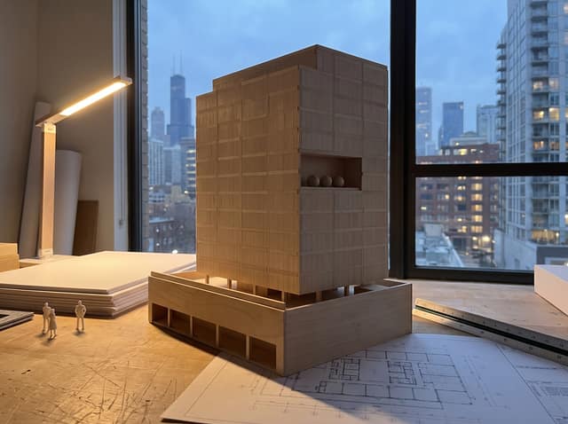 Visualization of a basswood massing model of Kinzie Exchange on a studio workbench at dusk.